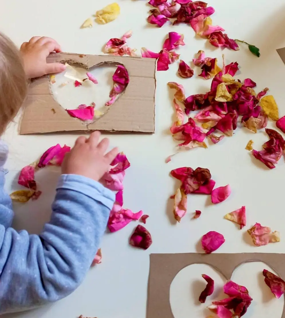 Bambino gioca con petali di rosa e sagome di cartone a forma di cuore