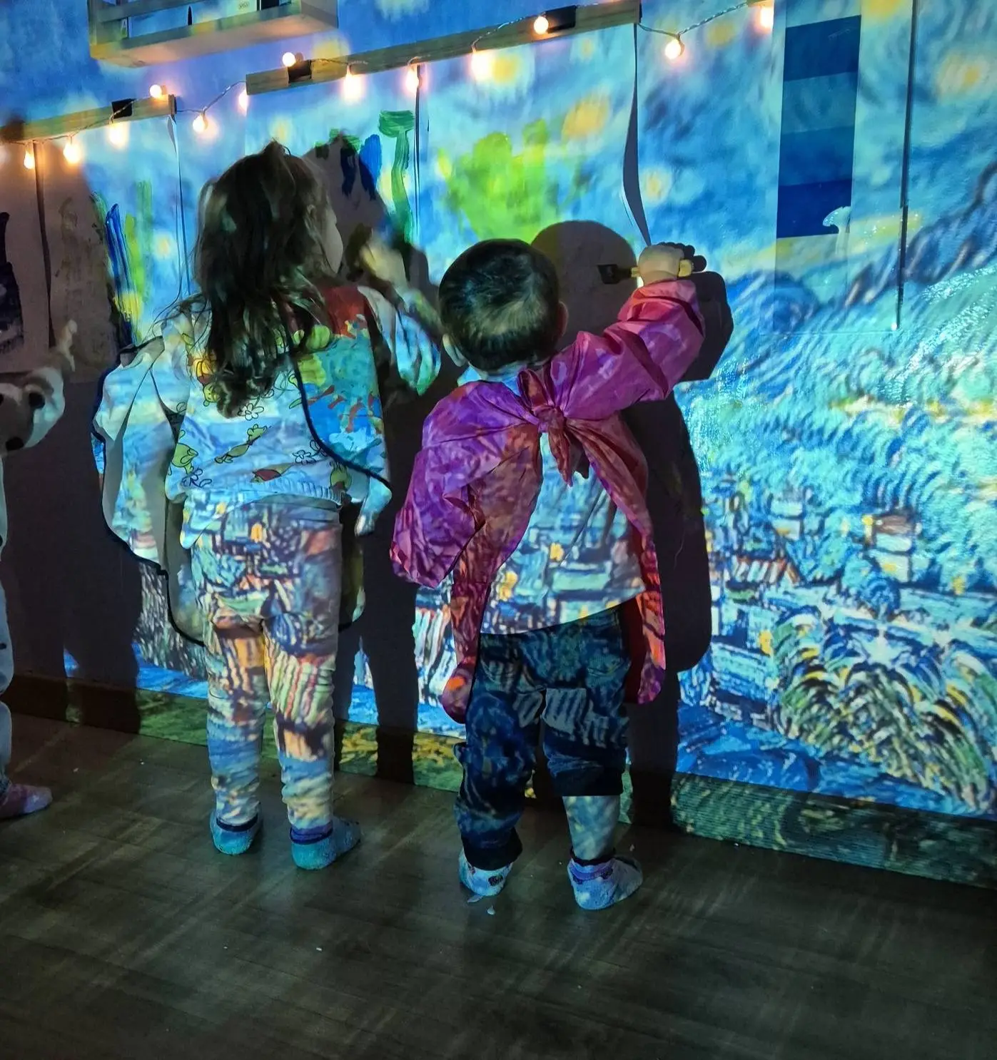 Bambini dipingono su una parete illuminata da proiezioni d'arte
